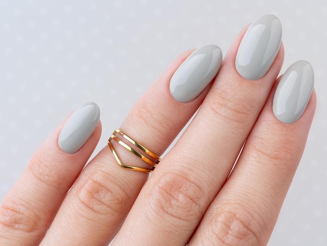 A photo of a woman's hand with a gray oval-shaped nails and a gold ring on it Desktop