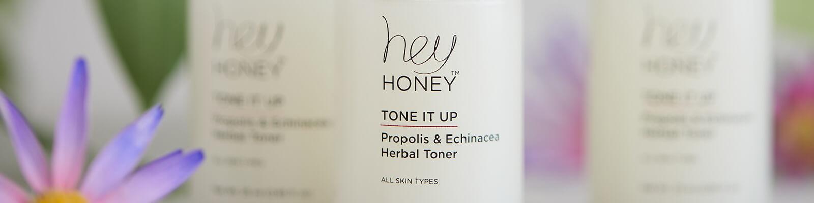 A close-up image of HEY HONEY Tone It Up! Propolis & Echinacea Herbal Toners and a purple flower Desktop