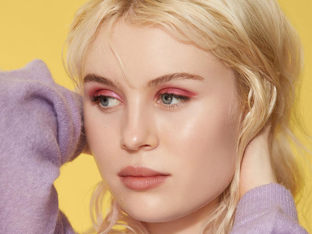 Blonde model posing and rocking a shimmery rose eyeshadow makeup look against yellow background Desktop