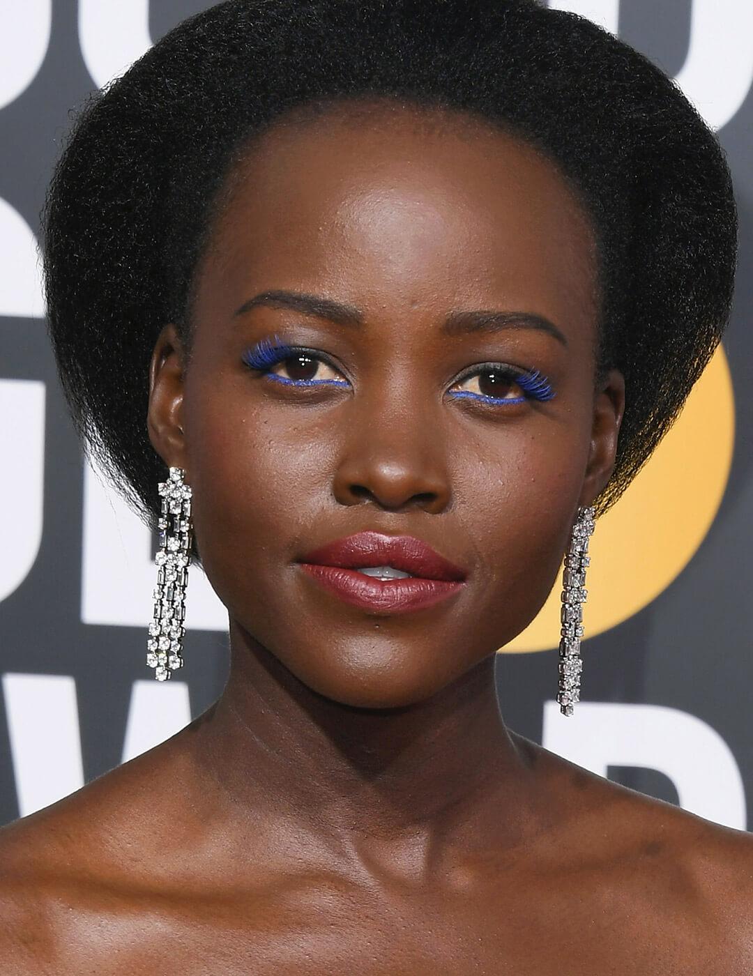 Lupita Nyong'o rocking a blue eyeliner and mascara makeup look and silver dangling earrings Desktop