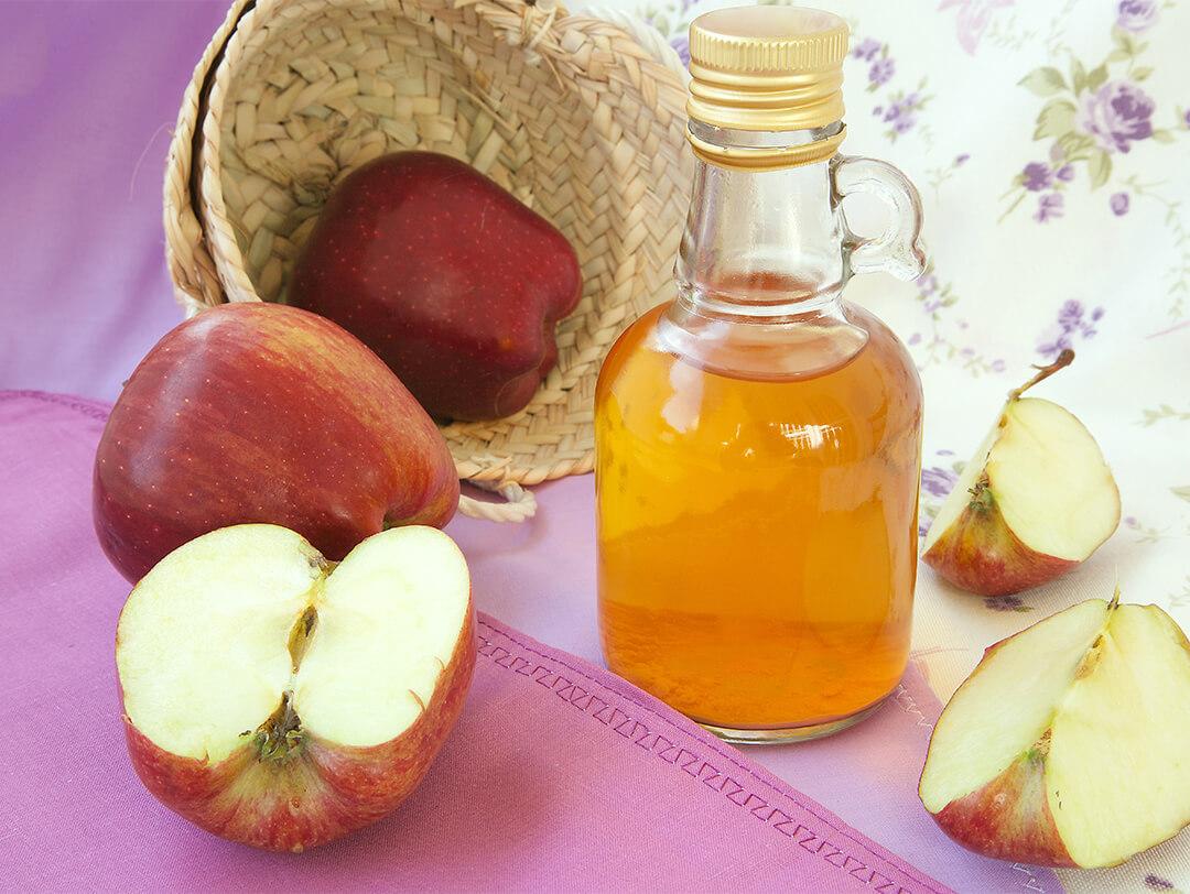 Flat lay image of sliced apples and a bottle of apple cider vinegar on purple and floral cloths Desktop