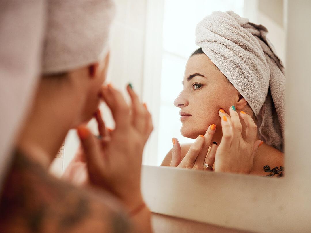 Image of a woman with hair wrapped in a towel checking a zit in the mirror Desktop