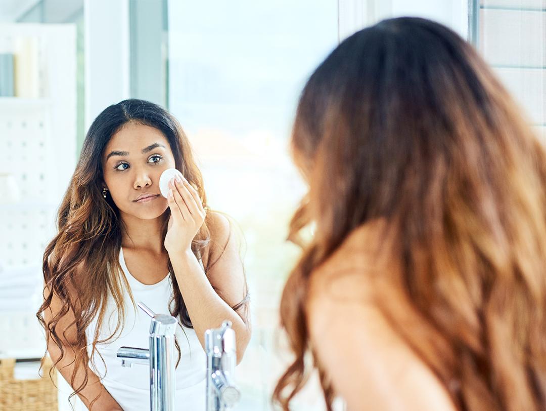 An image of woman with long hair in front of a mirror applying toner on her face Desktop