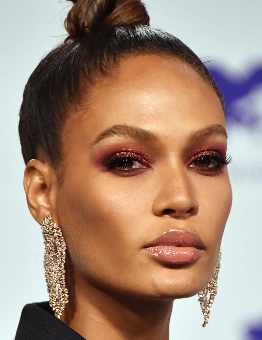 Close-up of Joan Smalls rocking a glittery red smoky eye makeup look, top bun, and gold dangling earrings Desktop