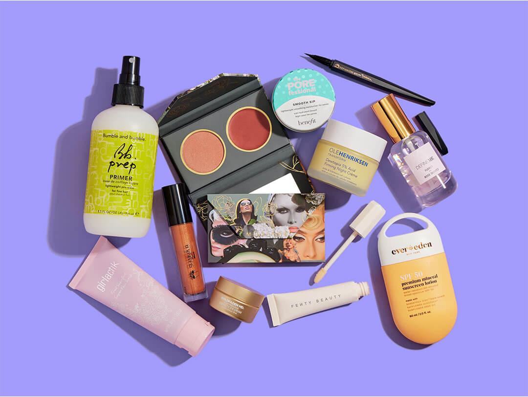 Skincare, makeup, and hair care products and tools from various brands scattered on purple background Desktop