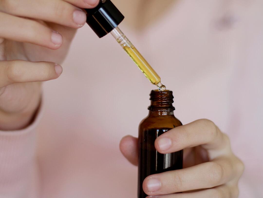 Close-up image of woman's hands holding a bottle and dropper of marula oil Desktop