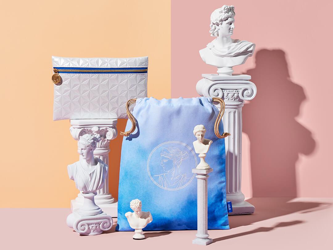 March 2023 IPSY Glam Bag and Glam Bag Plus bags with mini Roman bust sculptures against cream and rose background Desktop
