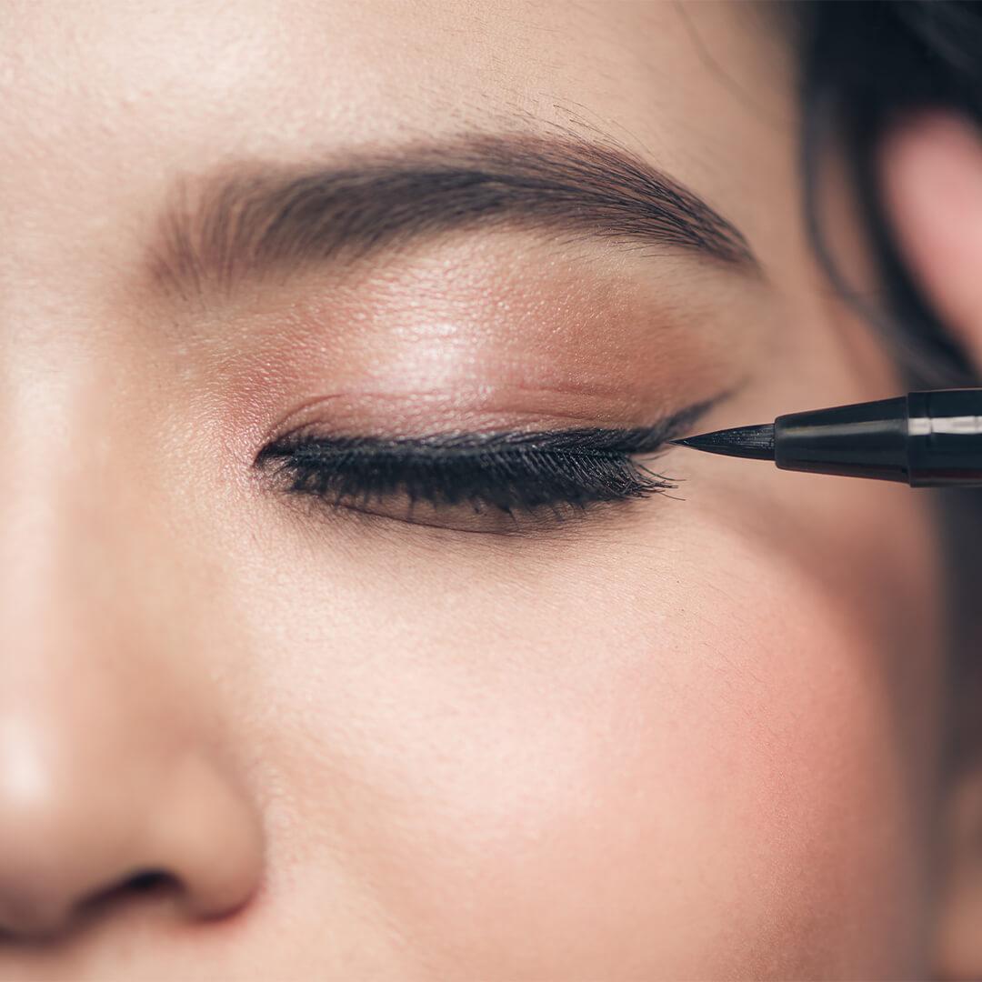 Close-up image of a woman with a neutral eyeshadow look applying liquid eyeliner Desktop