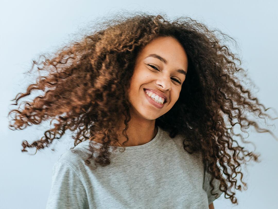 Young woman with curly hair in grey shirt smiling Desktop