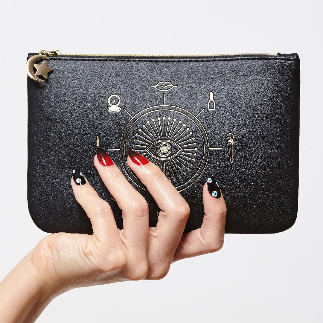 Close-up image of model's hand with black and red graphic nail art mani holding the IPSY October 2020 Glam Bag Mobile