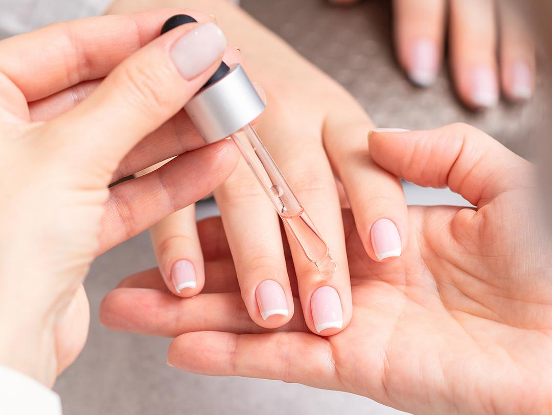 A closeup shot of hands of a manicurist pouring serum on her client's fingers Desktop