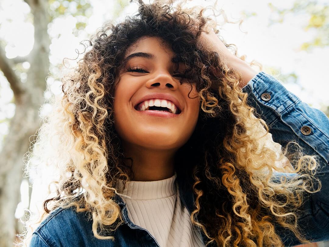 Curly-haired woman smiling and posing in the forest Desktop
