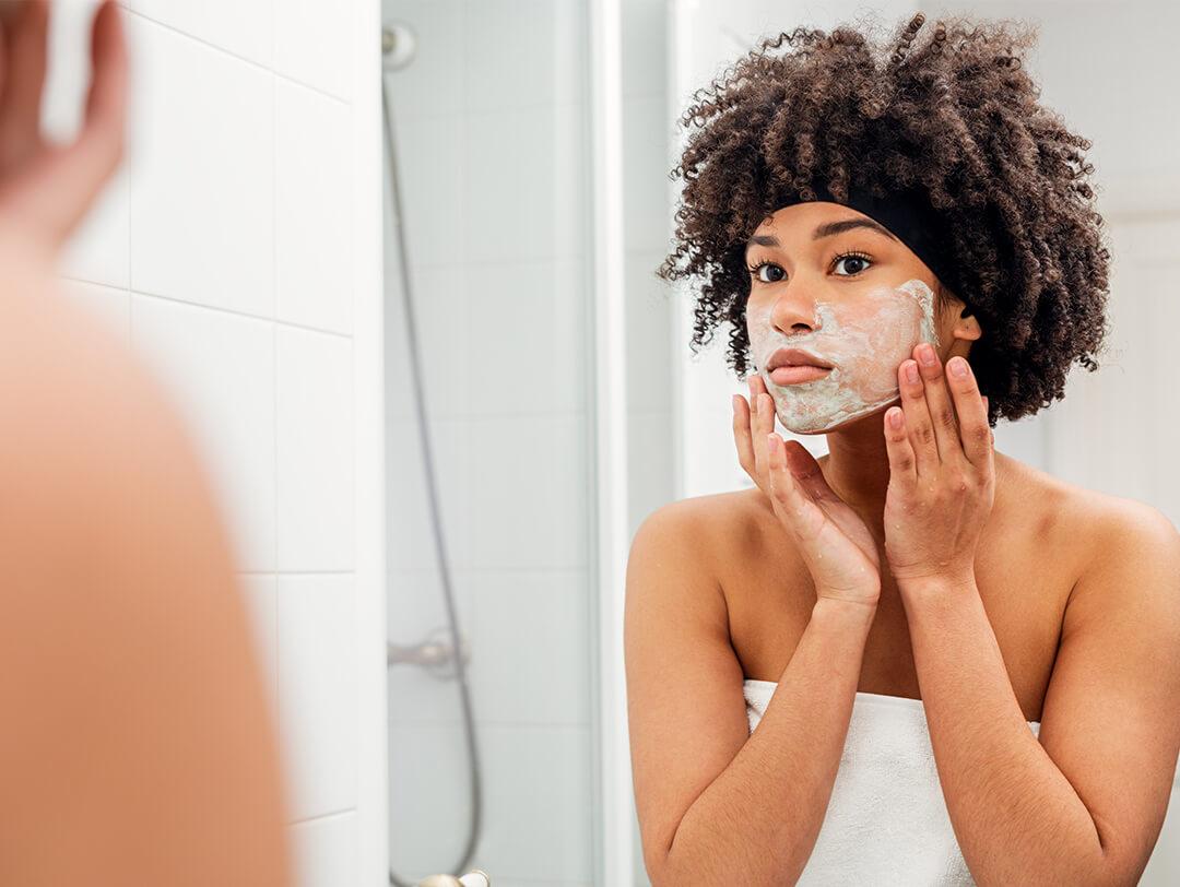 Young woman applying mask on her face while looking at herself in the bathroom mirror Desktop