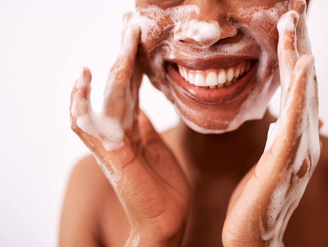 An image of a woman of color, smiling at the camera as she washes her face Desktop