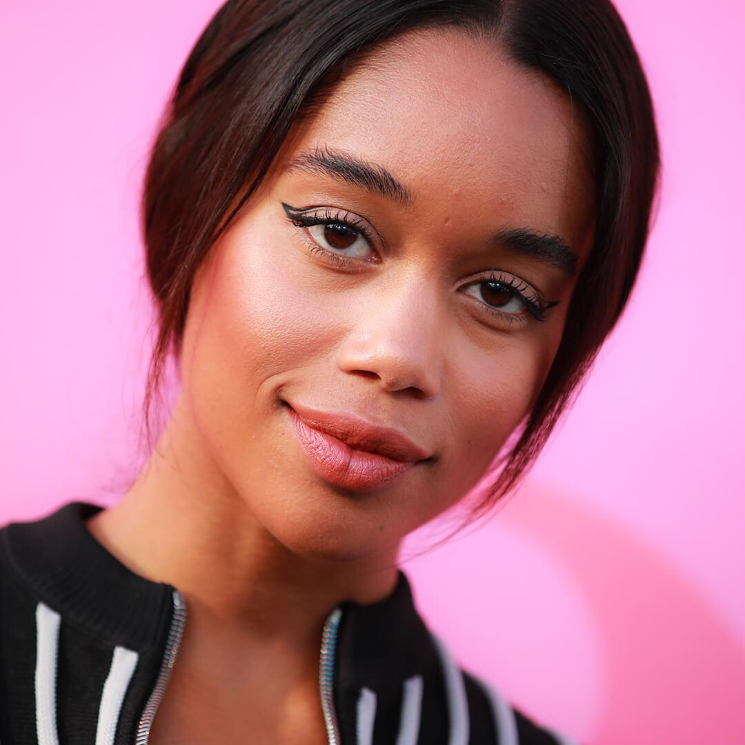 Laura Harrier rocking a graphic eyeliner makeup look on the red carpet against pink background Desktop