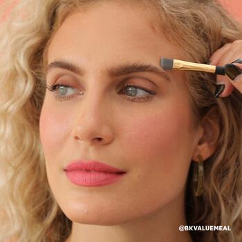 An image of a model blending concealer over her eyebrow with a smudge brush Mobile
