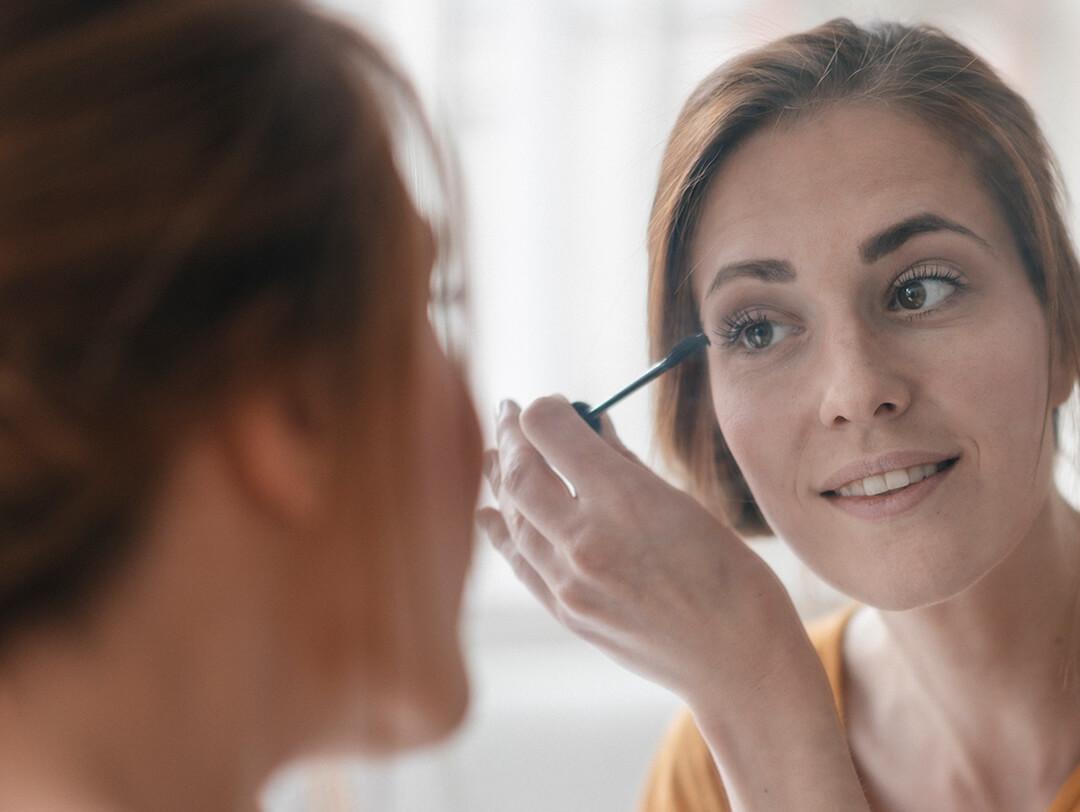 Woman applying mascara in front of a mirror Desktop