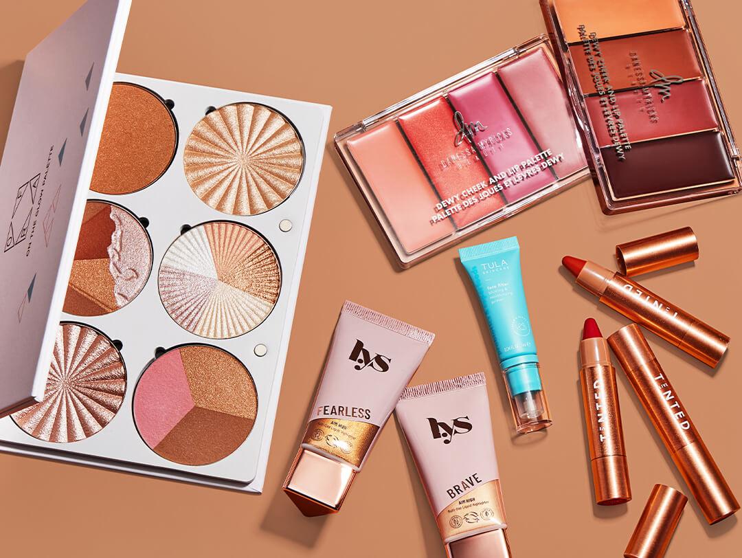 Makeup and beauty products from various brands scattered on brown background Desktop