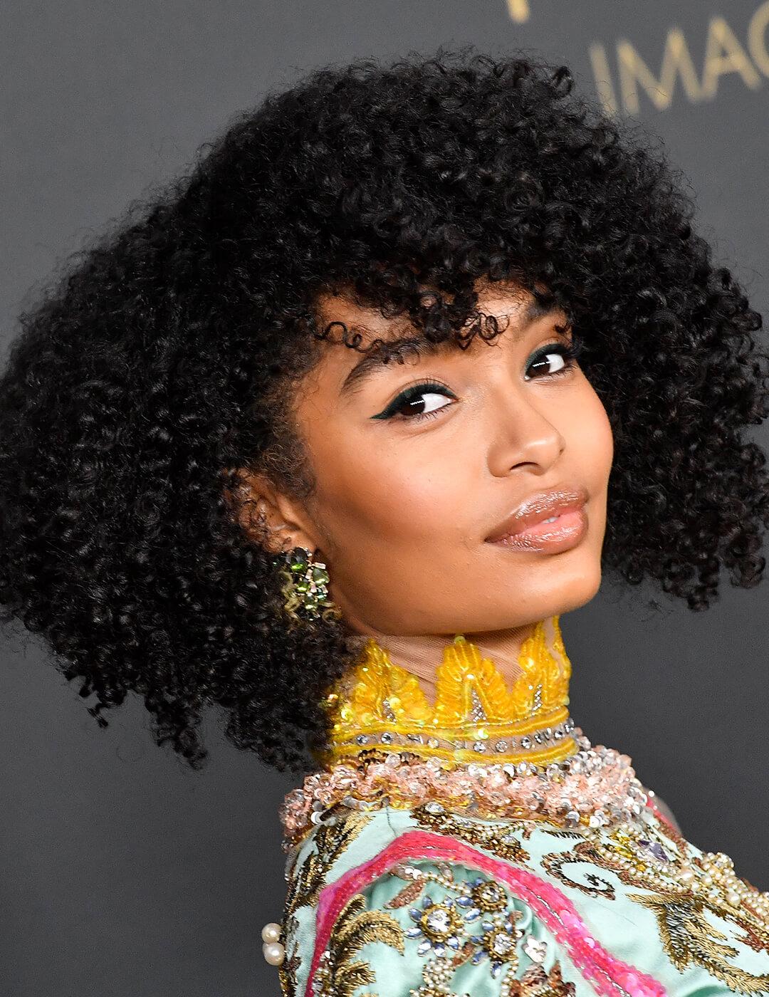 A photo of Yara Shahidi looking fabulous in her curly black bob hair with winged liner on a black background Mobile