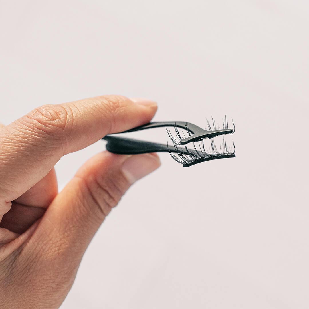 Close-up of a woman's hand holding false magnetic lashes using tweezers Desktop