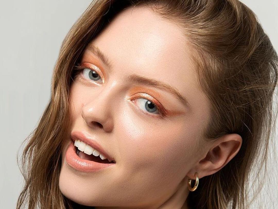 Close-up of a smiling young woman with copper eyeshadow makeup look Desktop