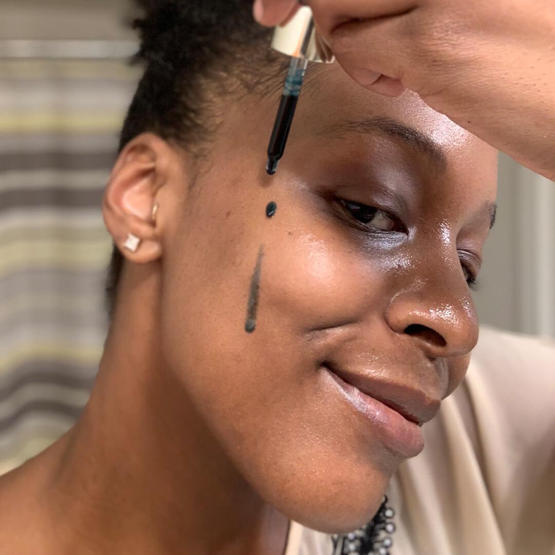 Close-up image of a woman putting blue oil on her cheek with a dropper Desktop