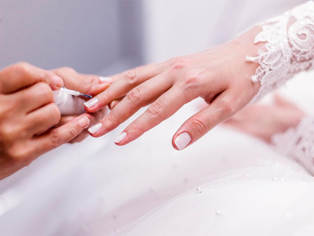A closeup photo of someone applying a coat of pearly white nail polish to a bride's hand Desktop
