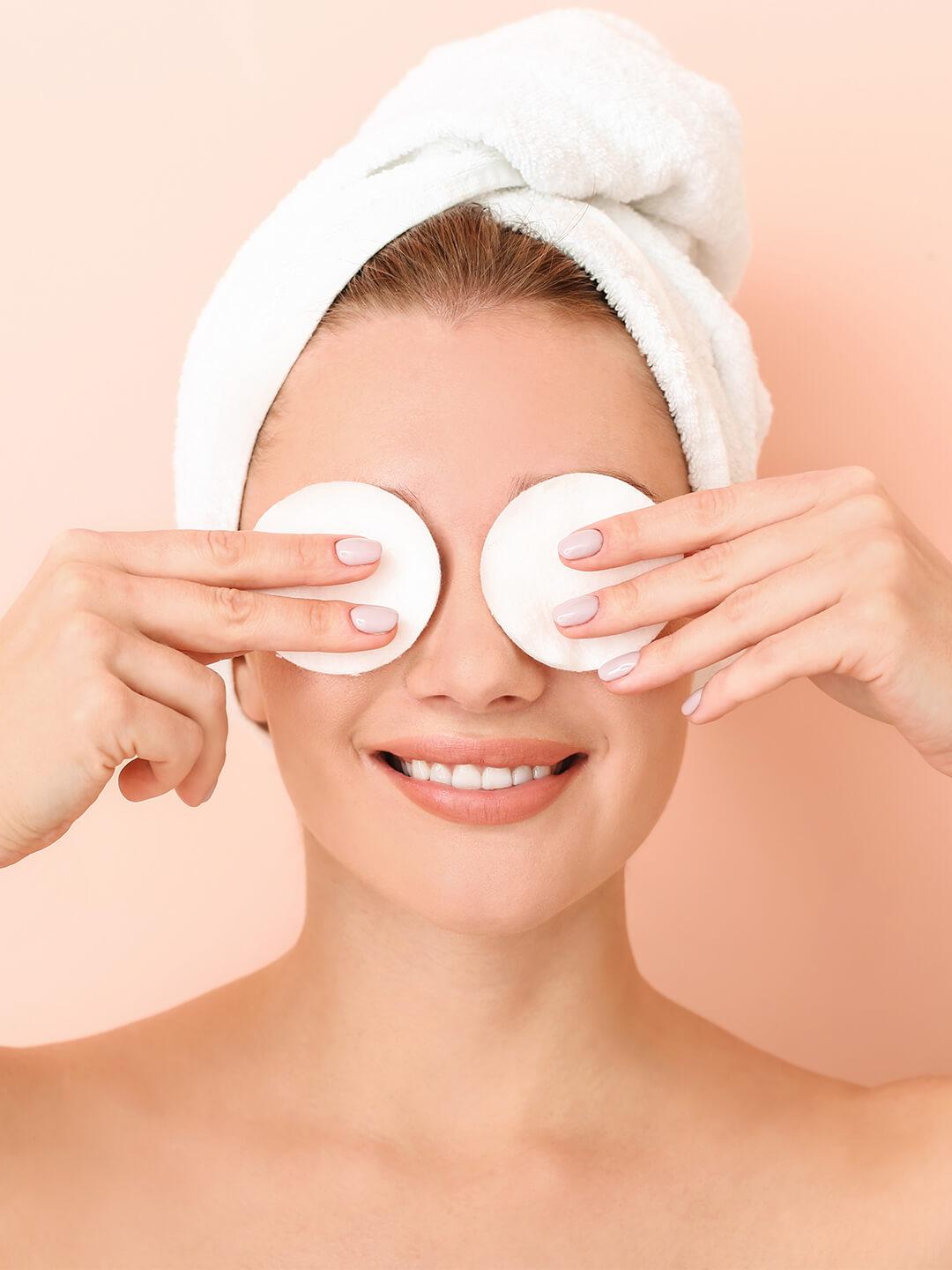Close-up of a woman with hair wrapped in a white towel and covering her eyes with cotton pads Desktop