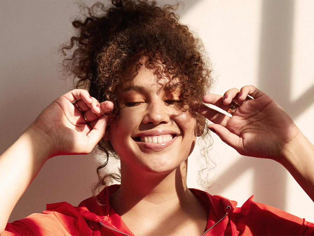 Close-up image of a model with curly hair posing with a big smile and closed eyes Desktop