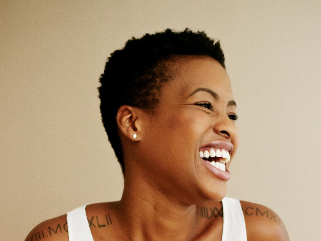Side profile image of a black woman with short hair in a white tank top laughing Desktop