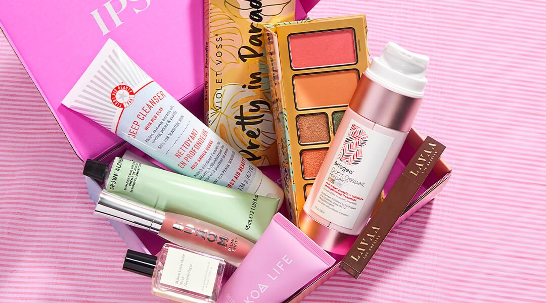 Skincare, makeup, and hair care products and tools from various brands scattered on pink background Desktop