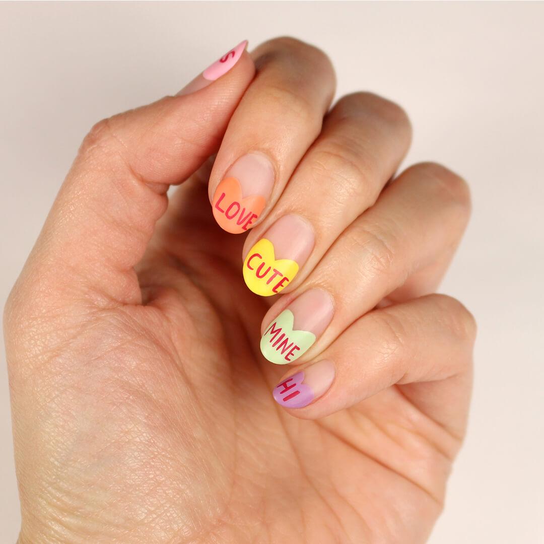 Close-up image of a woman's hand with colorful heart and text nail art Mobile