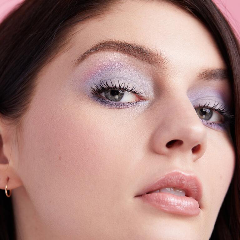 A close-up image of a model wearing a matte pastel blue and pink eyeshadow look paired with a nude pink lipstick Desktop