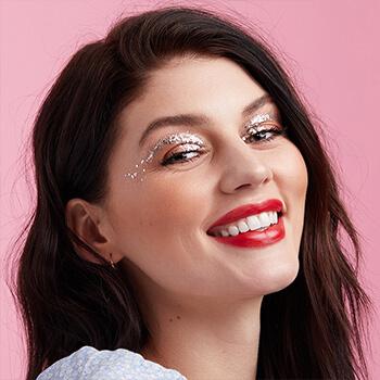 A close-up image of a model wearing nude eyeshadow with silver glitter gel arches paired with a bold red lipstick Mobile