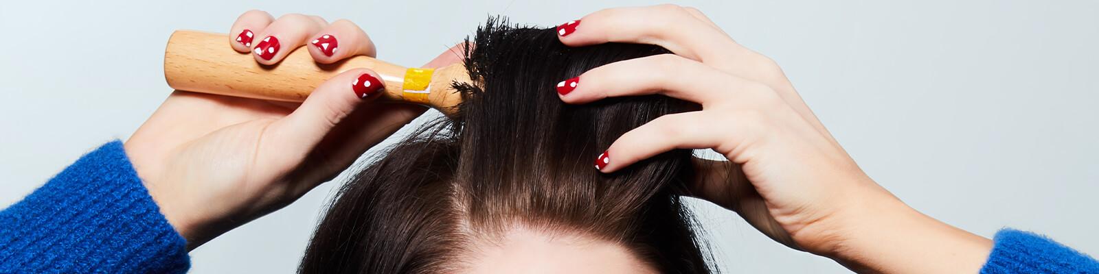 A closeup image of a model wearing blue knitted top brushing her hair with a round brush Desktop