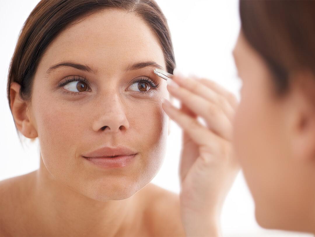 Close-up image of a woman plucking her eyebrows with a tweezer in the mirror Desktop