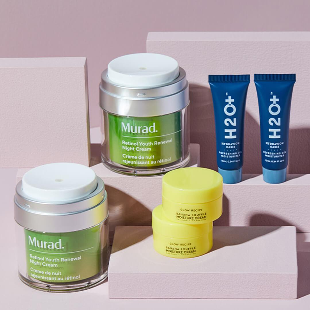 Two jars of MURAD Retinol Youth Renewal Night Cream, two pots of GLOW RECIPE Banana Souffle Moisturizer Cream, and two tubes of H2O+ Hydration Oasis Refreshing Gel Moisturizer on small mauve boxes against mauve background Desktop