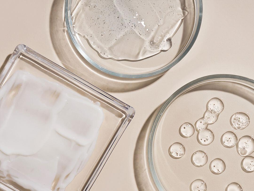 An up-close visual featuring a selection of cosmetic items such as hyaluronic acid drops, cream, and gel, displayed with smears for a detailed view Desktop
