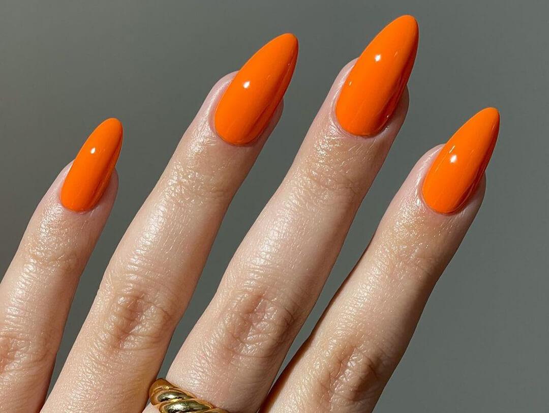 Close-up of woman's hand with gold ring and orange nail polish against dark grey background Desktop