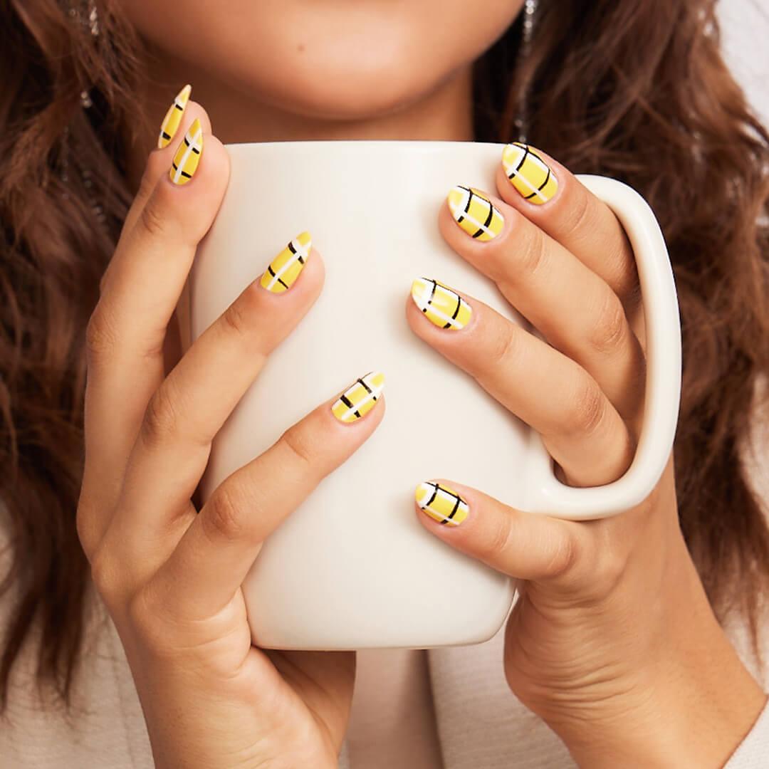 Close-up of a model's hands with yellow plaid nail art holding a white mug Desktop