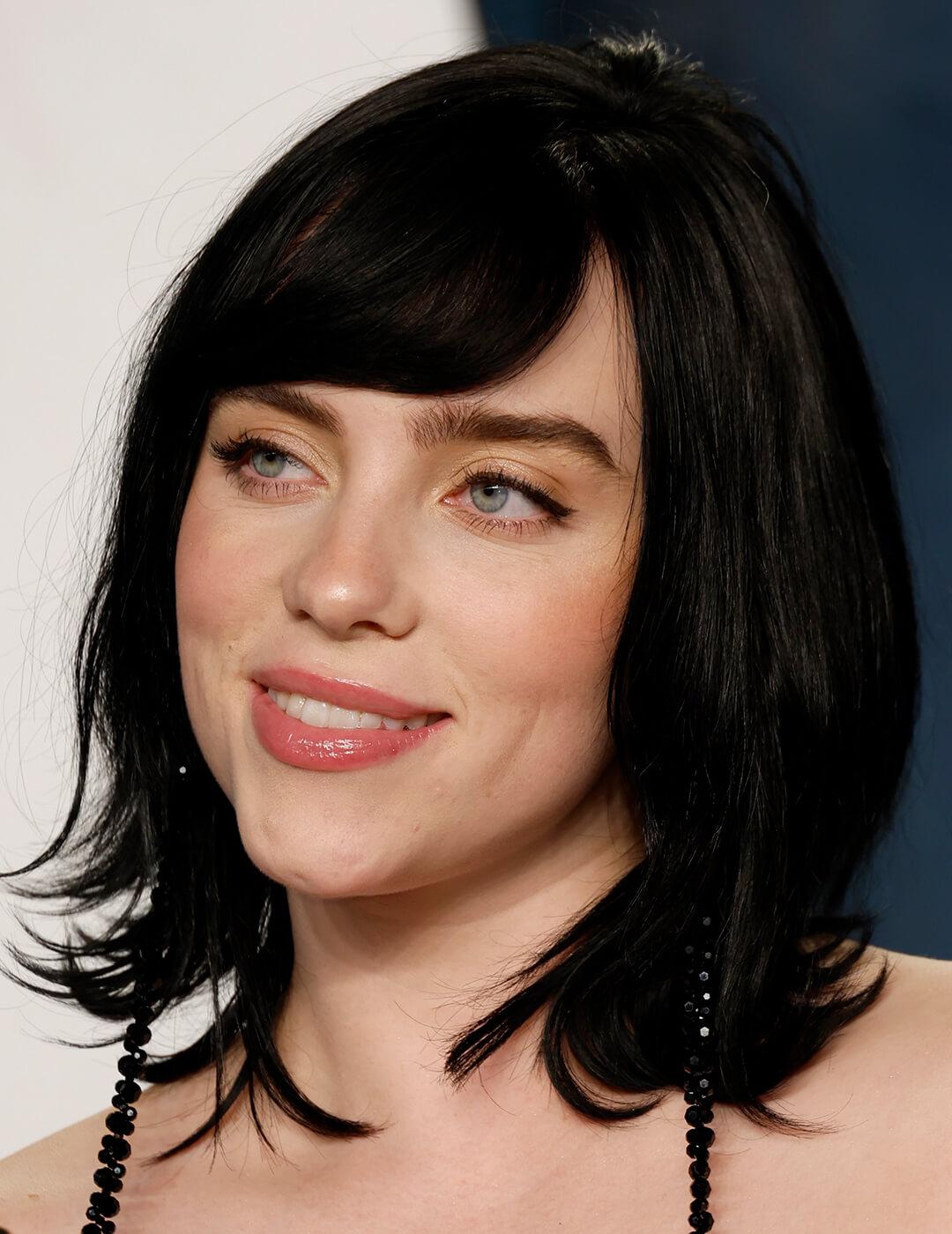 A photo of Billie Eilish with her black medium-length bob cut while looking and smiling sideways Desktop