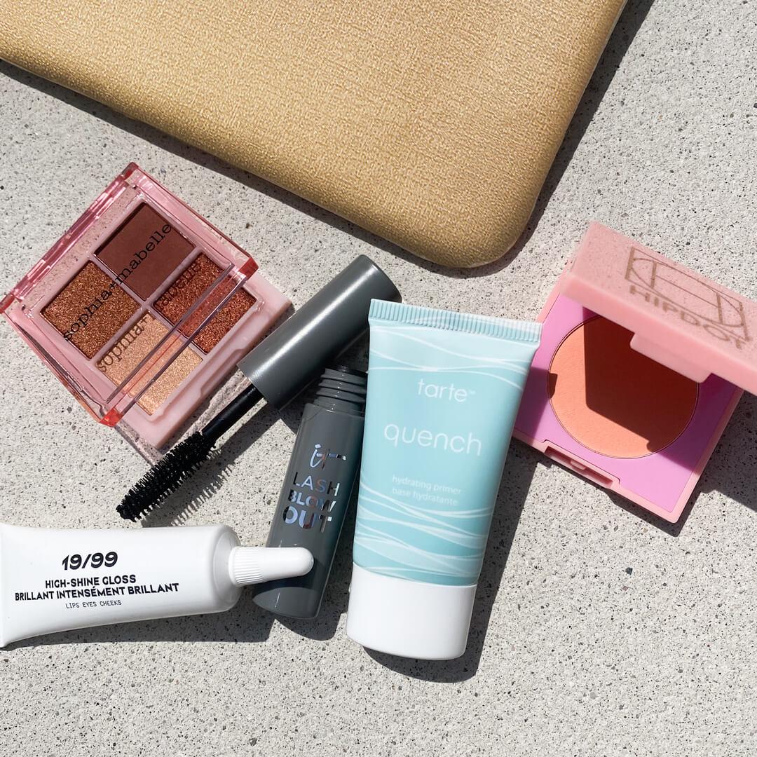 Gold-speckled makeup pouch with beauty products from various brands on concrete surface Desktop