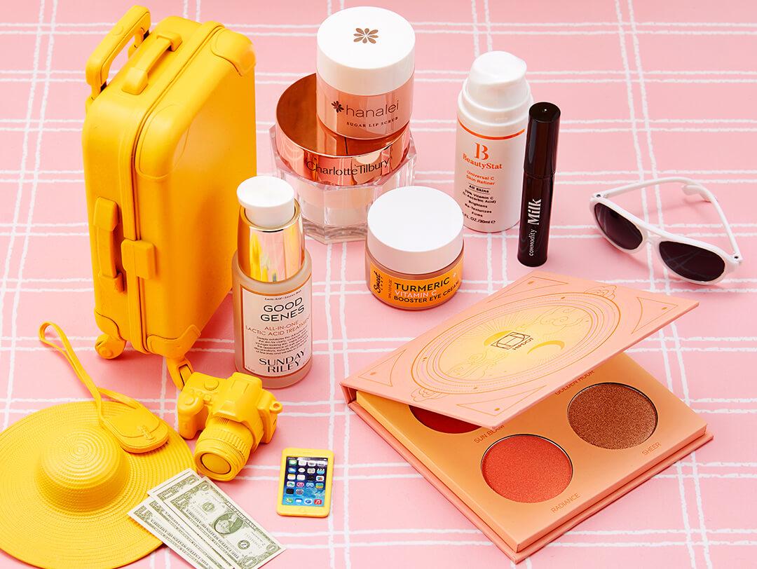 Flat-lay image of skincare and makeup products with miniature yellow luggage, hat, camera, iPhone, and dollar bills on pink and white tiles background Desktop