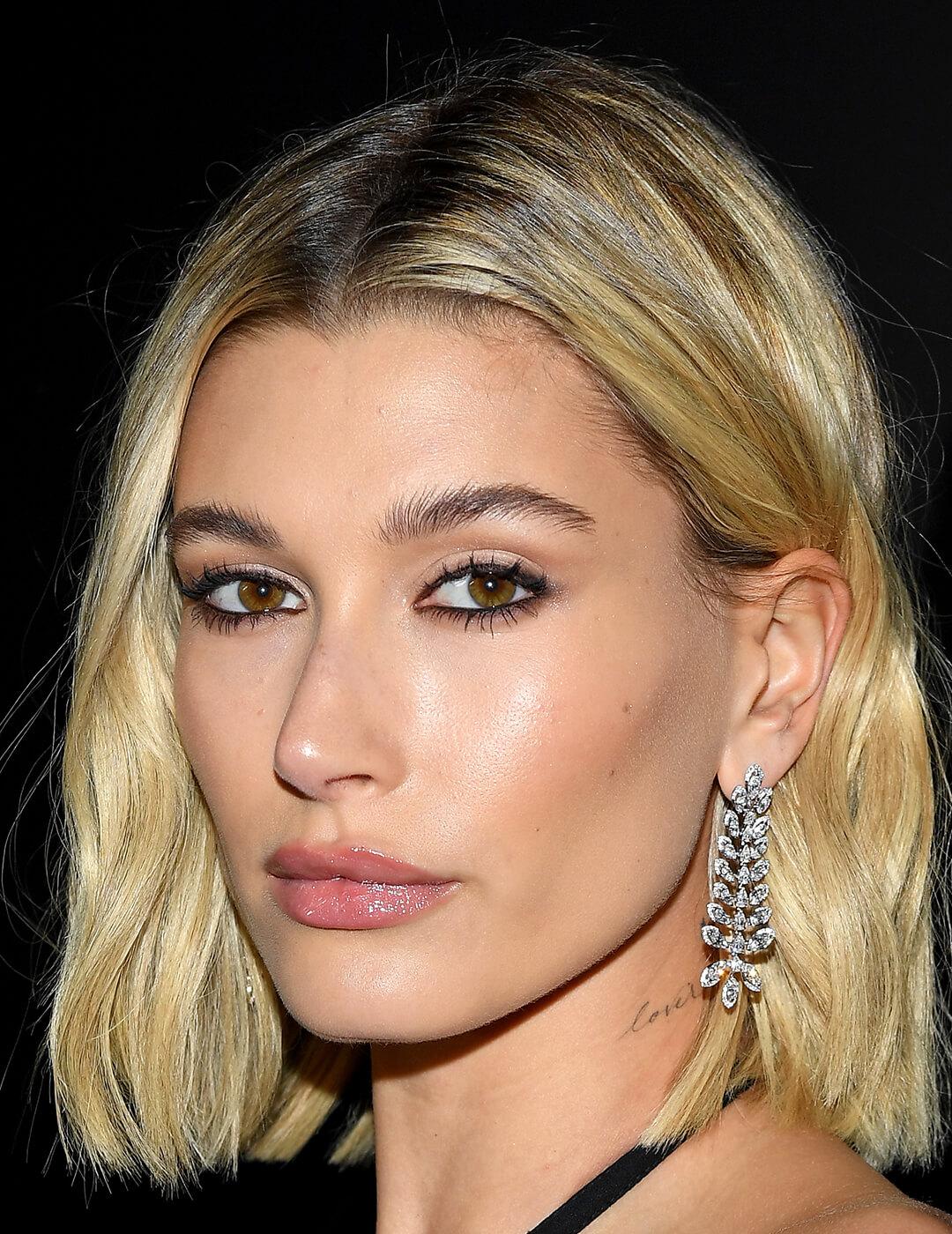 A photo of Hailey Bieber with her hair tucked in her ear showing her dazzling silver earring Mobile