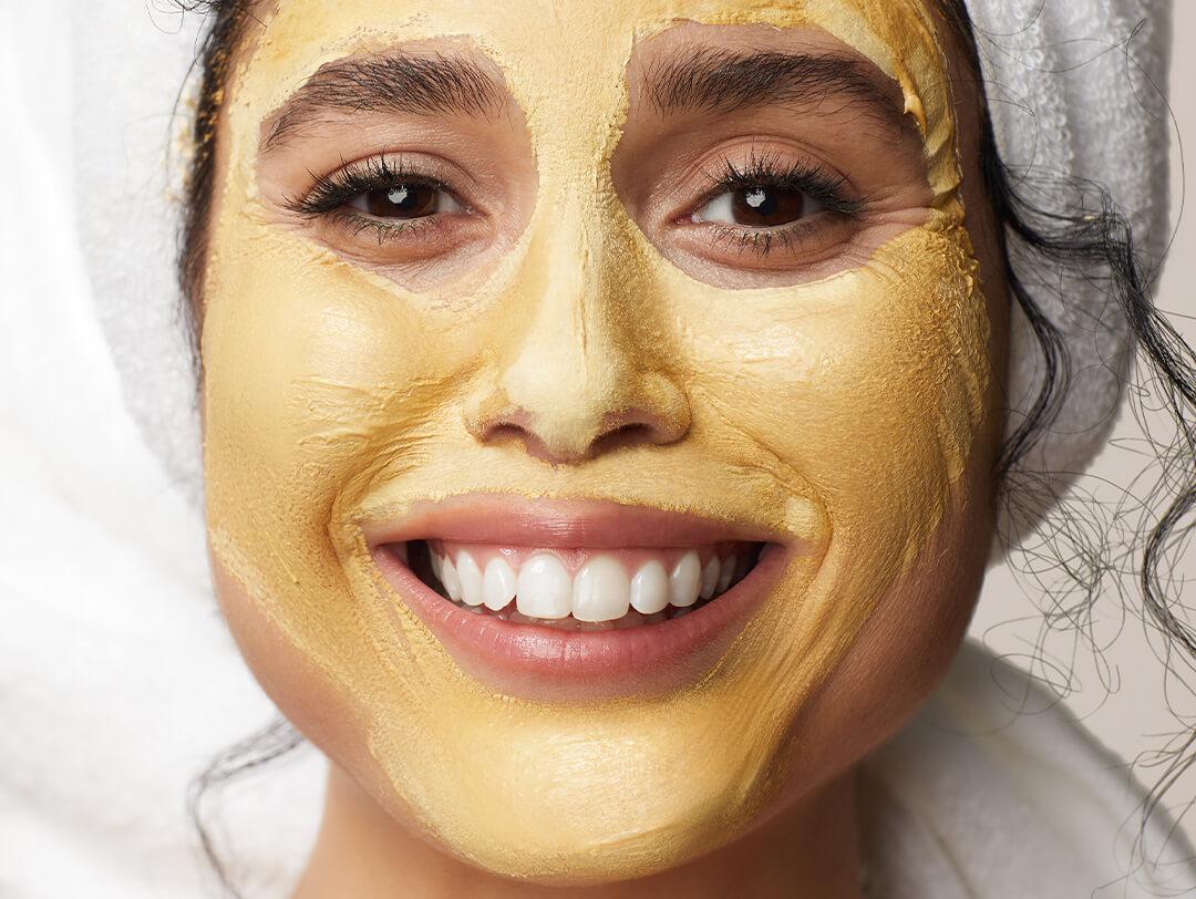 Close-up of a model with her curly hair wrapped in a white towel and yellow colored face mask on her face Desktop