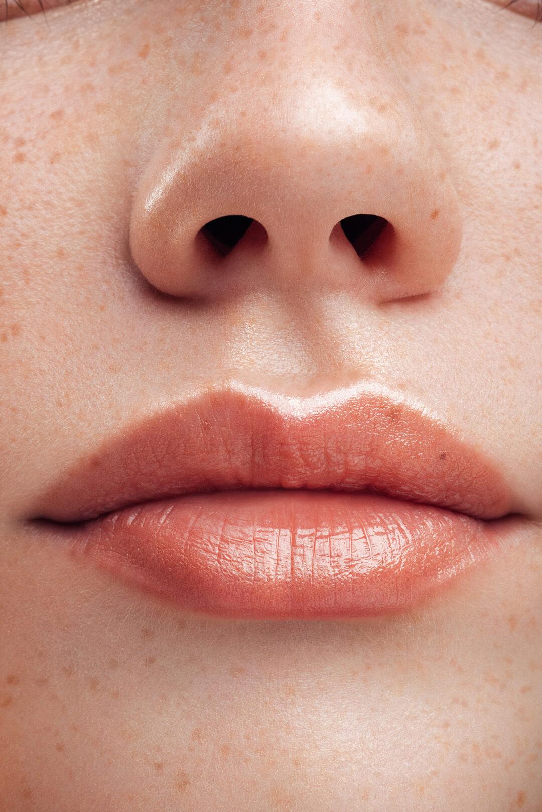 A close-up image of a woman's lips and nose displaying her charming freckles wearing a sheer lipgloss Desktop