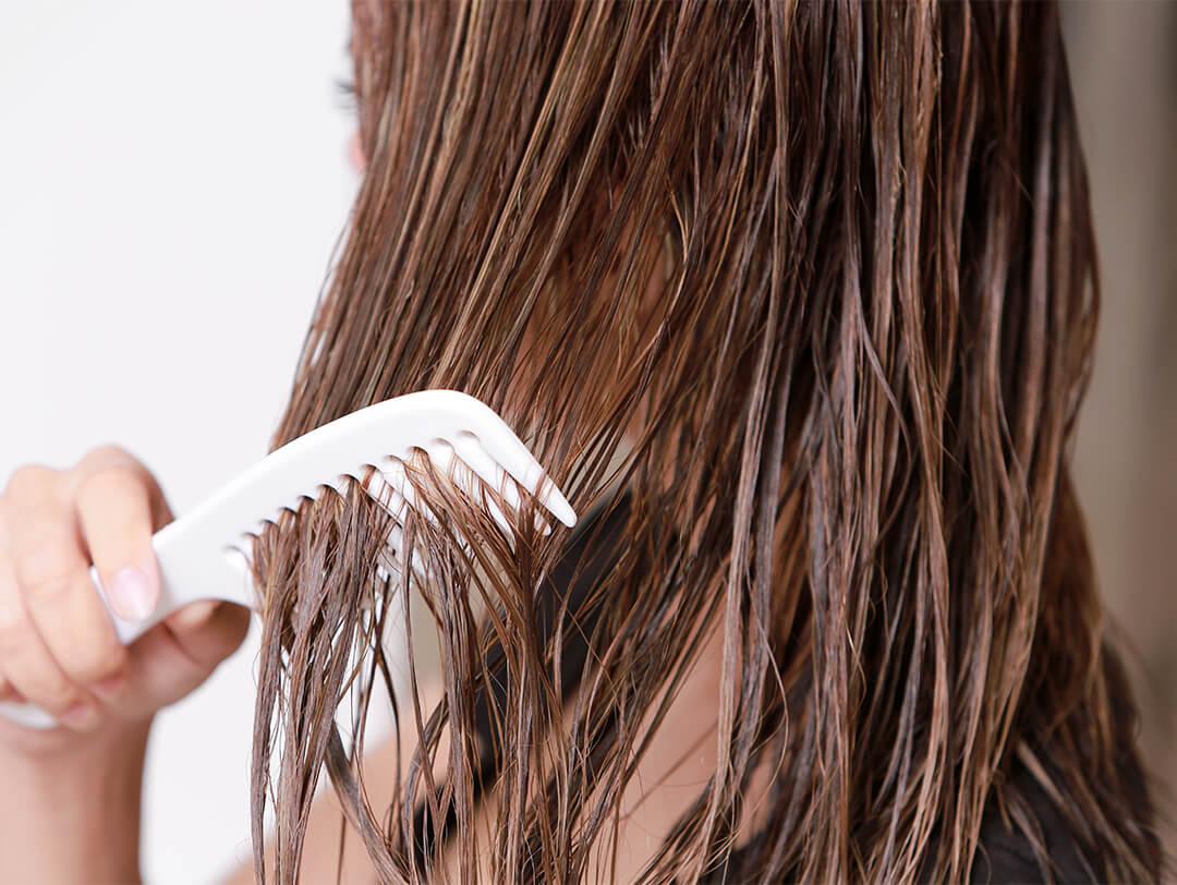 Close-up image of a woman combing her wet brown hair with a white comb Desktop