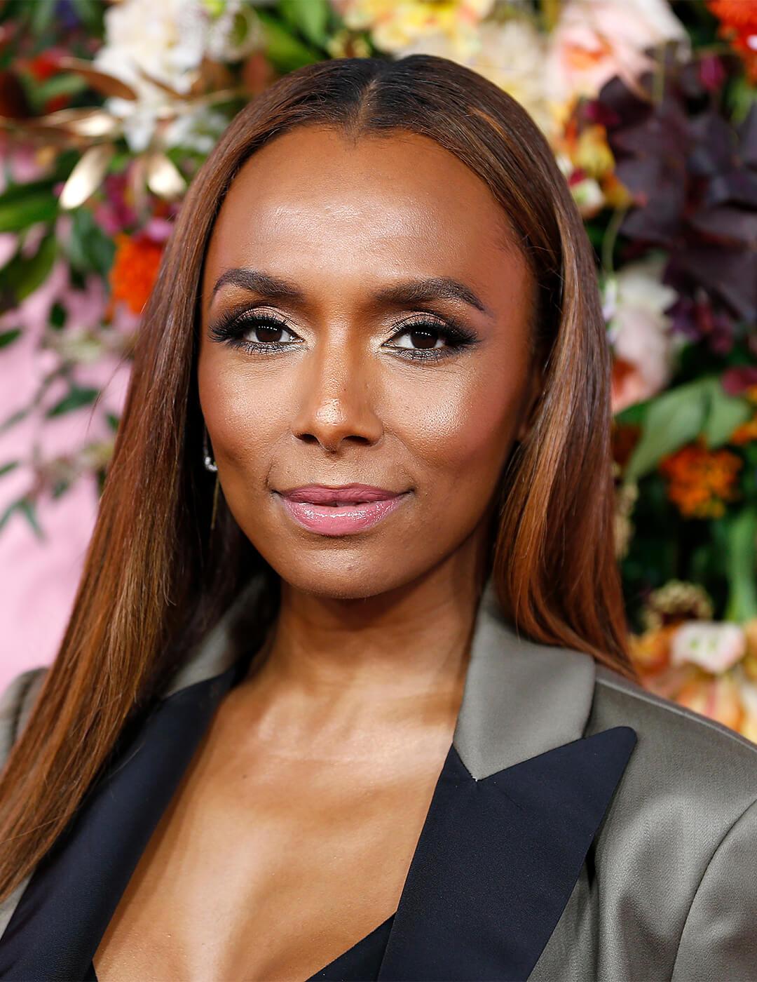 Janet Mock in a grey suit smiling against flowers background Mobile