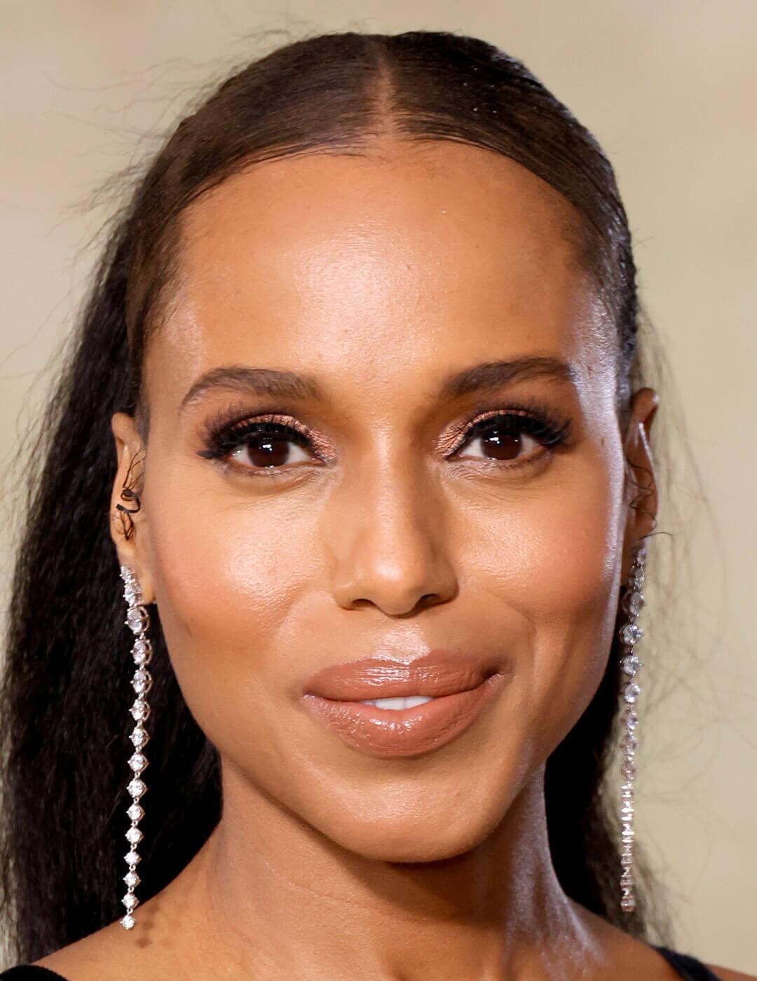 A close-up image of Kerry Washington wearing a red, white paint-streak-esque pattern and a black velvet upper trim, and a plunging neckline, wearing subtle makeup with her deep-set eyes adorned with a diamond dangling earings Mobile
