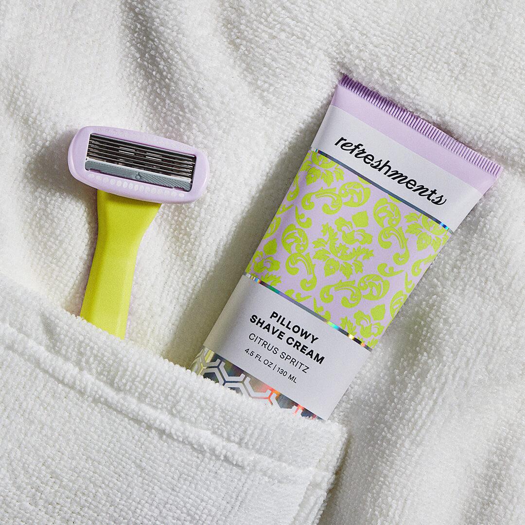Close-up of the REFRESHMENTS Dazzling 5-Blade Razor and REFRESHMENTS Pillowy Shave Cream inside a bathrobe pocket Desktop